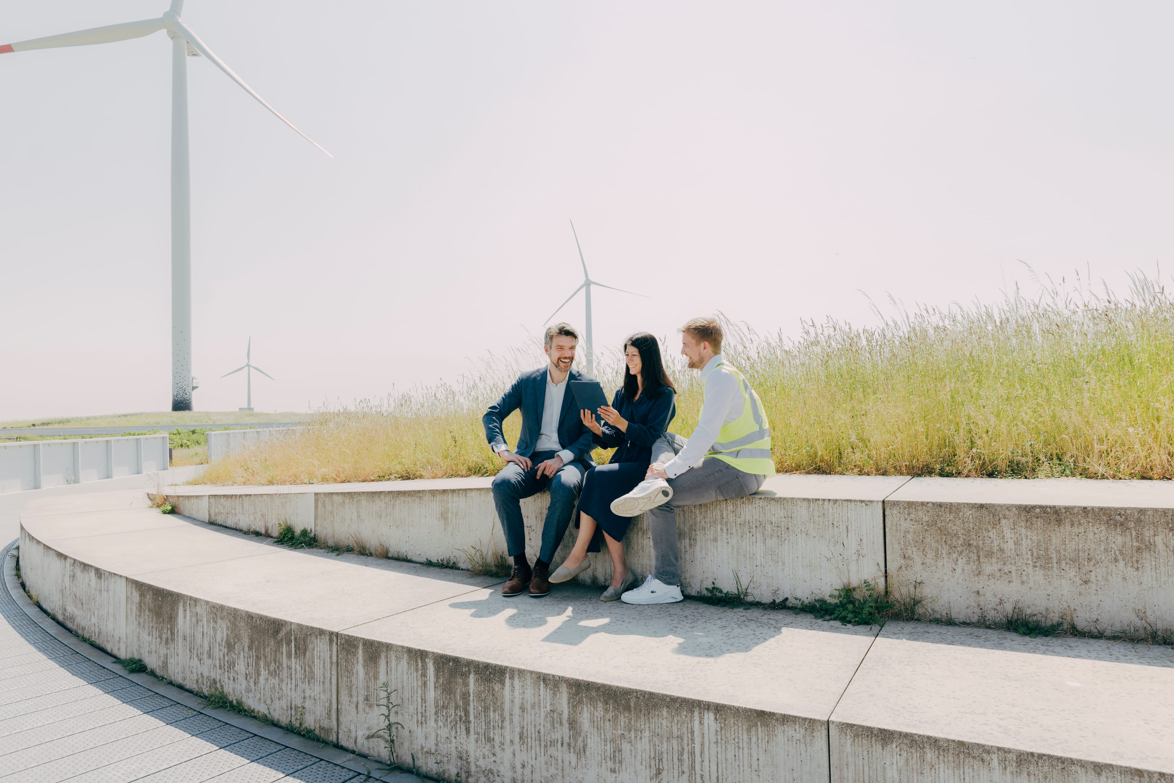 Brandingfoto – Erneuerbare Energien – drei Mitarbeitende in Gesprächssituation outdoor vor Windrädern